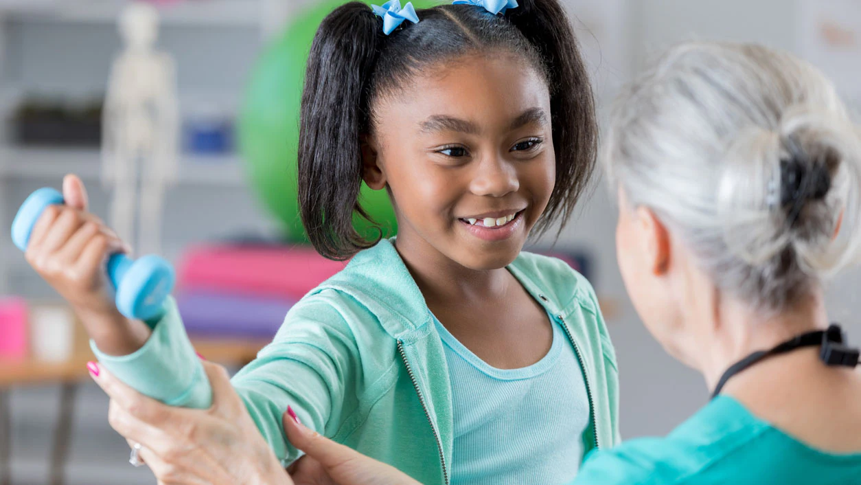 Young child with arthritis lifting dumbbells during physical therapy.