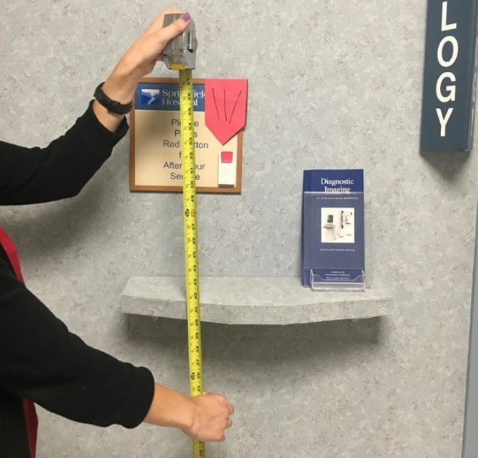 a person measuring the height of a sign in a mammography clinic to ensure it is accessible to all patients.