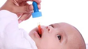 A mother using a dropper to give a baby a vitamin supplement.