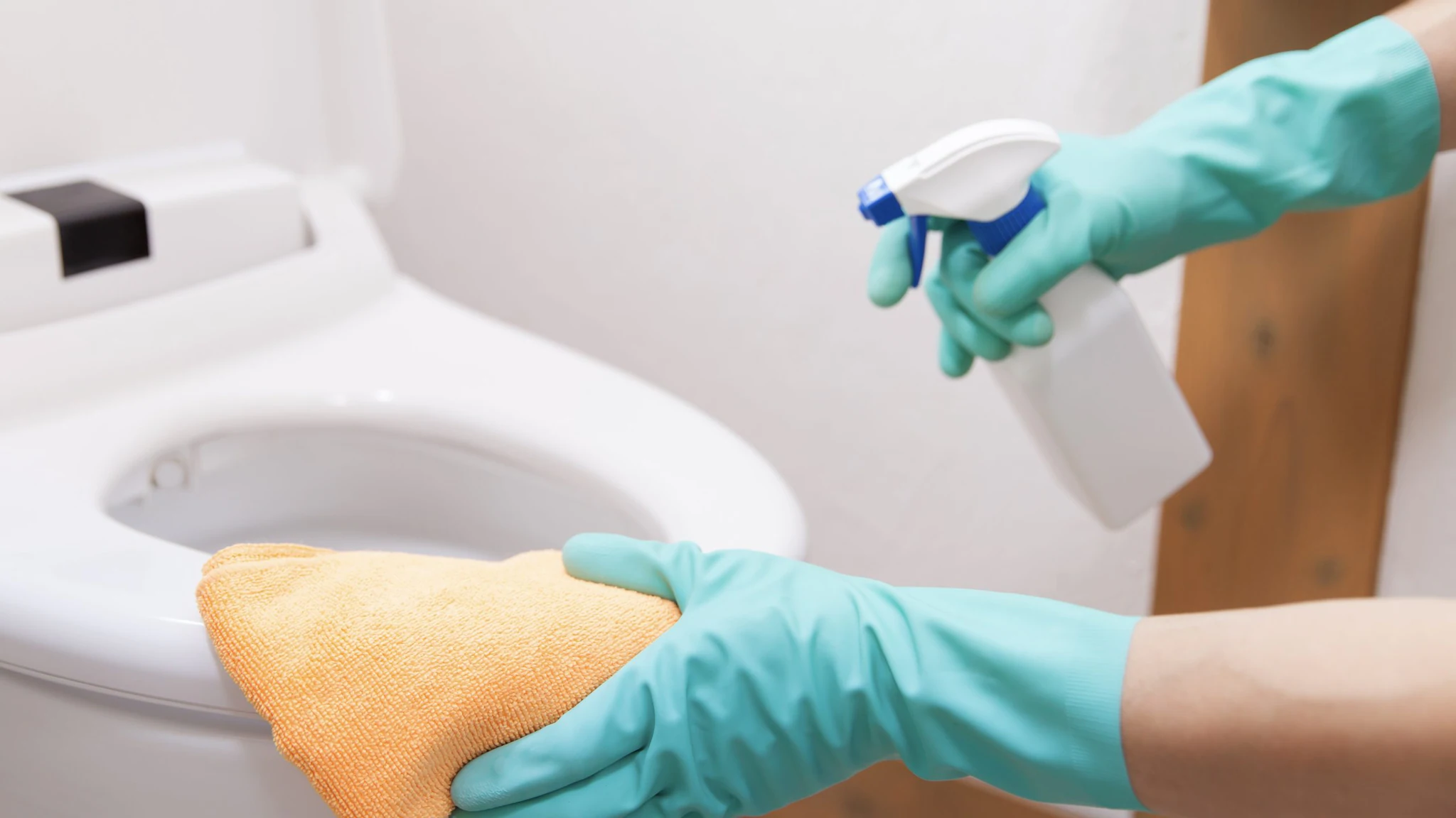 Gloved hands holding a rag and spray bottle while cleaning a toilet