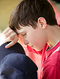 Young boy, holding a cap and wiping his brow.