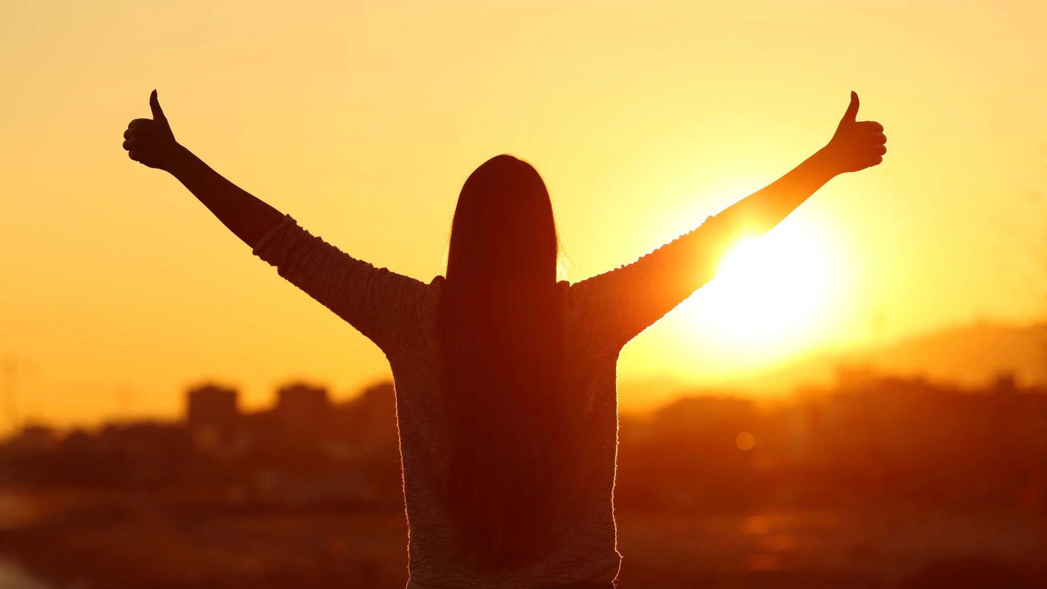 Woman standing and facing the sun with two thumbs up