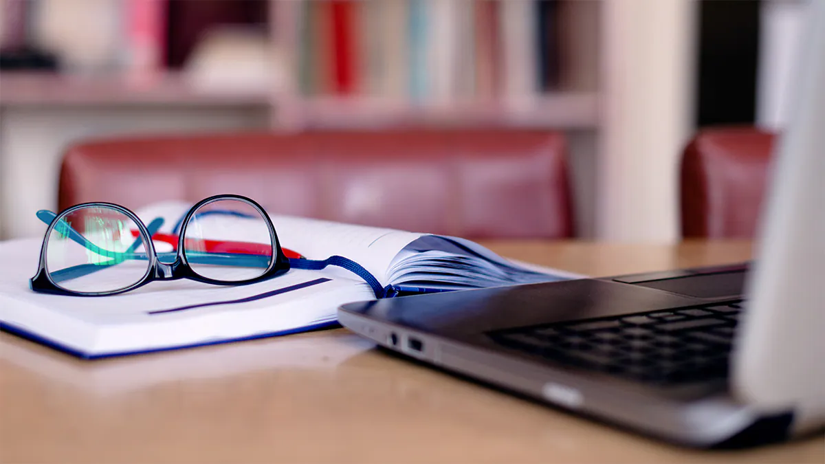 Glasses and notebook next to a laptop