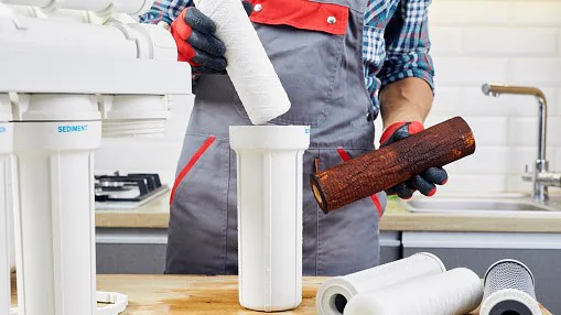 A person wearing gloves taking out a dirty filter membrane from a water filter system and putting in a new, clean filter.