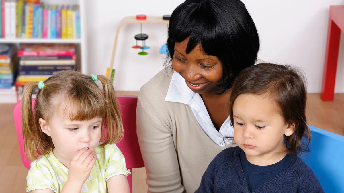 An early care and education provider sits at a table with children eating fruit.