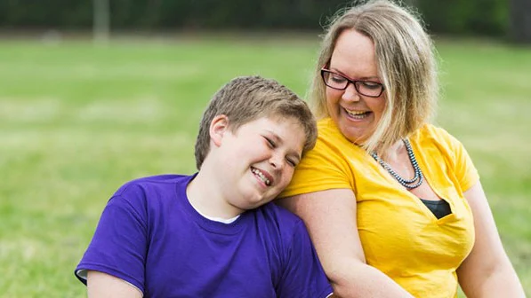 Mother and son leaning on each other outside at a park.