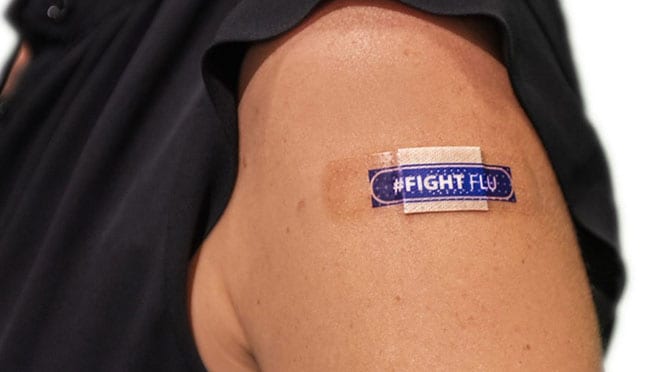 A person is wearing a black shirt and has a bandage on their upper arm that reads "FIGHT FLU."