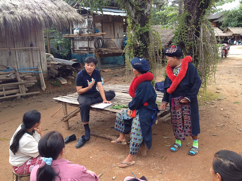 A male health professional speaking with community members outside in rural Thailand.