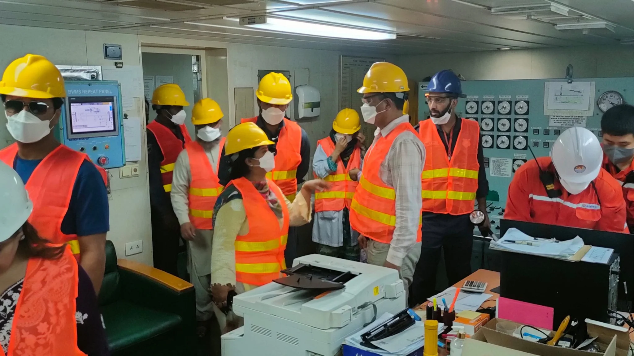 inspection of the master control room on vessel, room filled with people wearing high vis gear