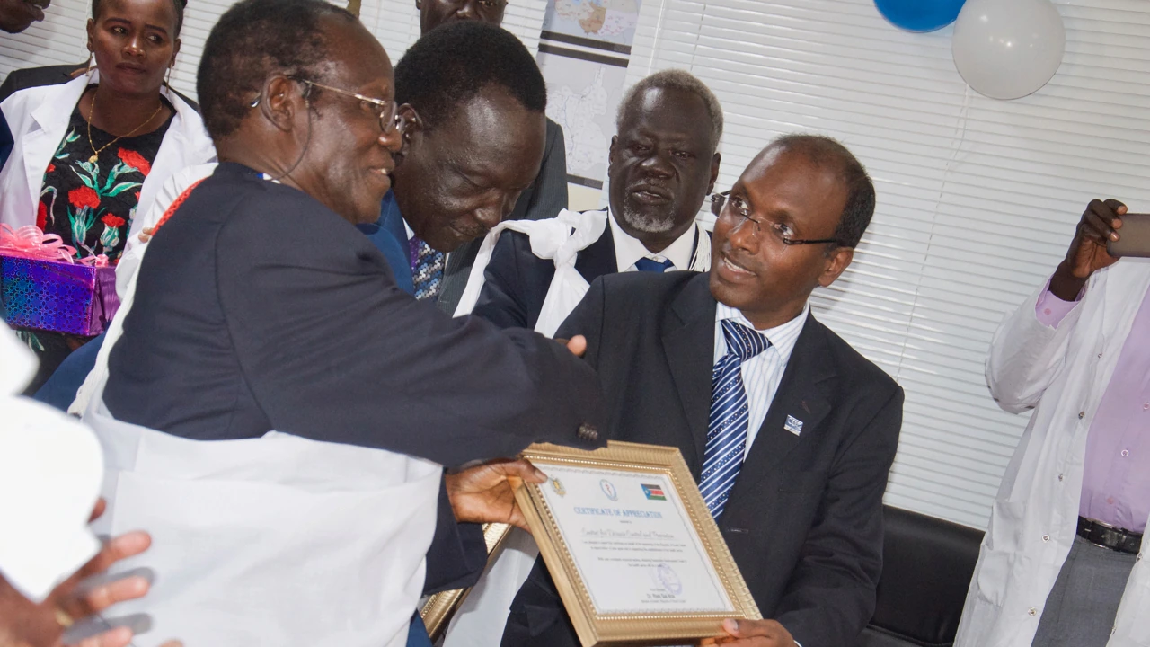 Two people hold a framed certificate of appreciation. Other people look on nearby.