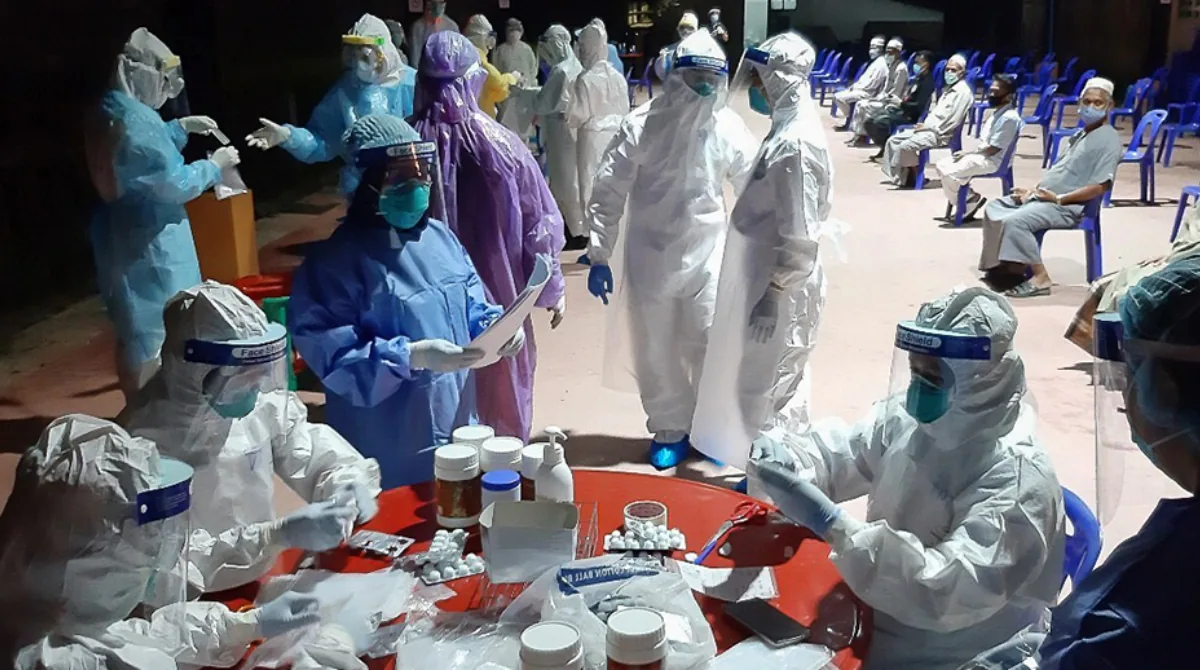 Health care wokers in PPE and individuals waiting in chairs waiting to be seen.