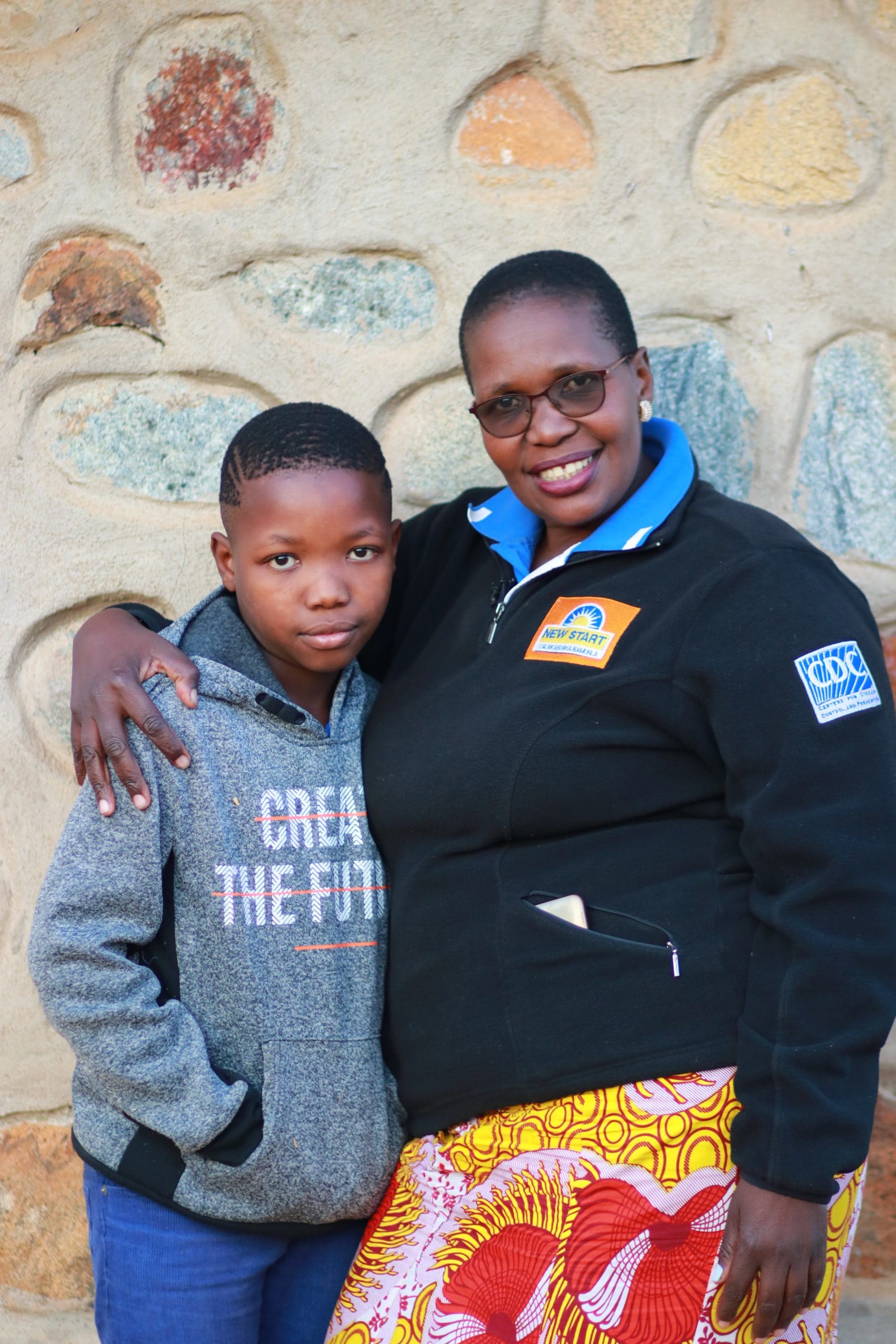 Mother and son stand together smiling.