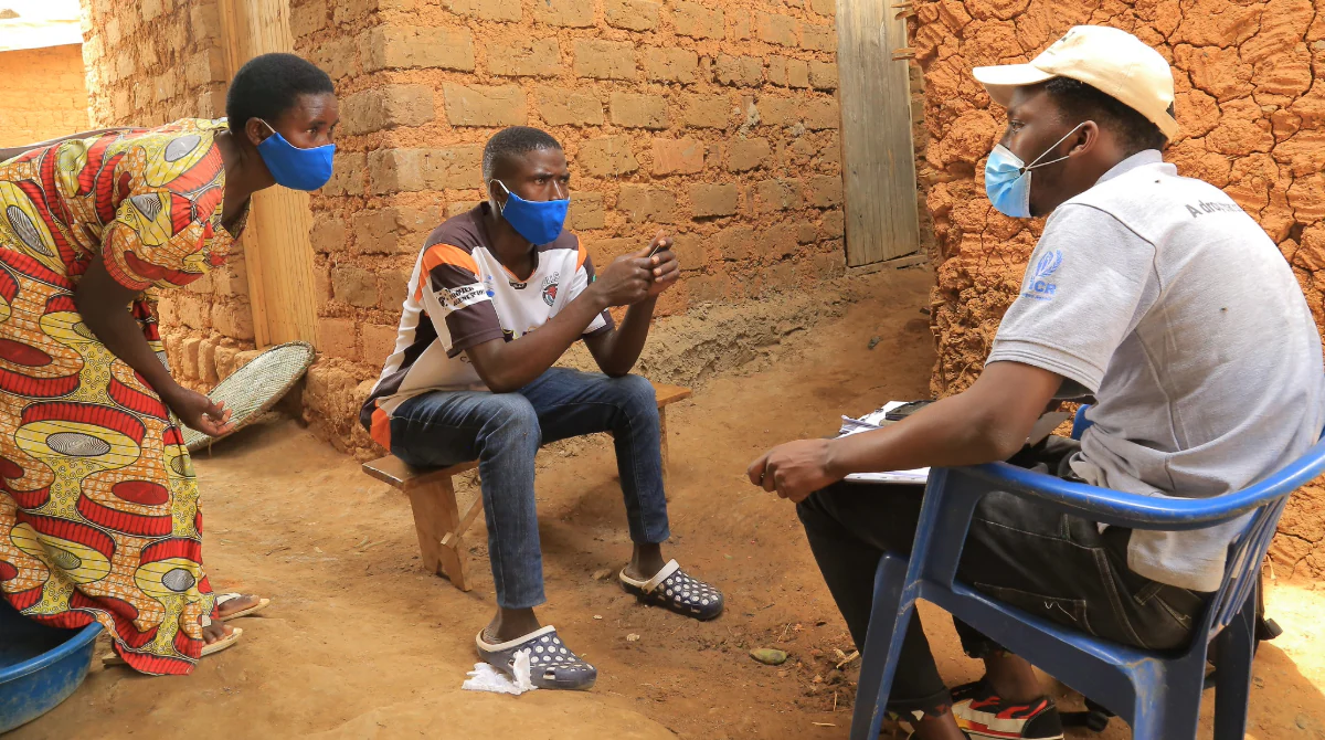 Man interviews a man and woman in a Uganda community.