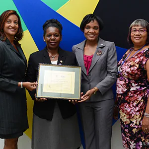 Four women stand in front of a colorful background, holding a certificate.