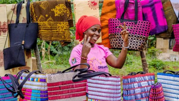 A young woman in pink stands at with bags she created.