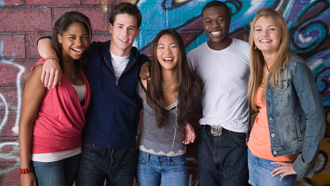 A group of high school students standing together in a classroom, smiling and laughing.