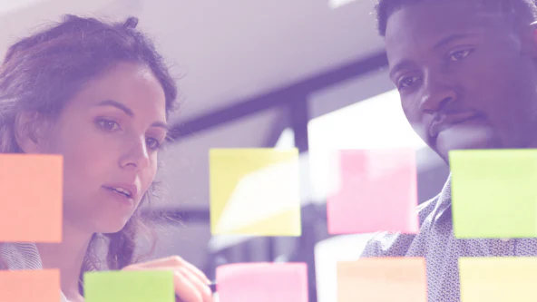 A female teacher and male teacher looking at and organizing Post-it notes.