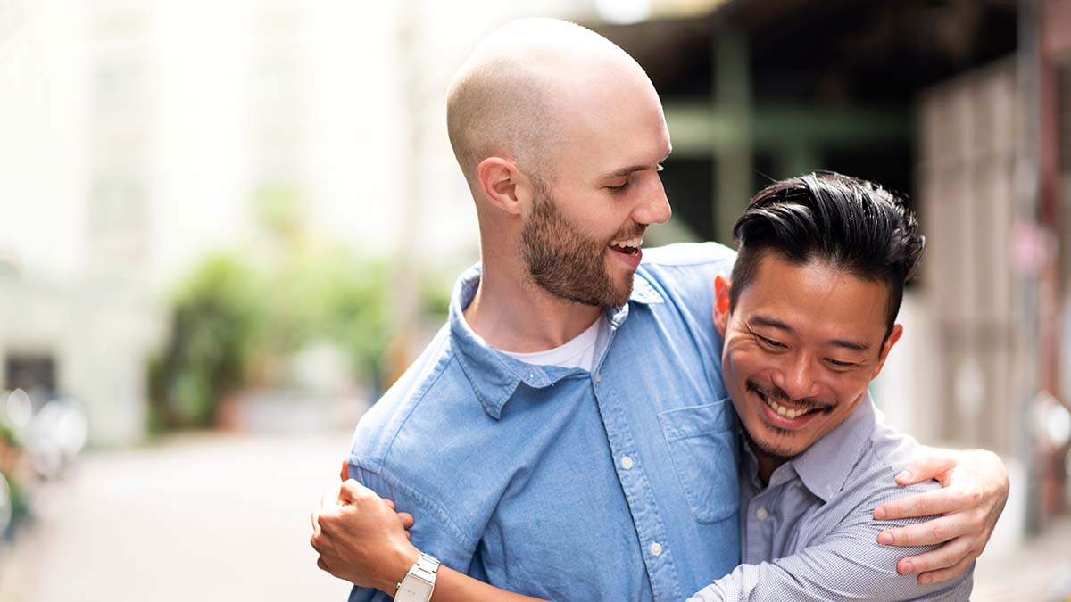 Two gay men vaccinated against hepatitis a and hepatitis b hugging walking down the street