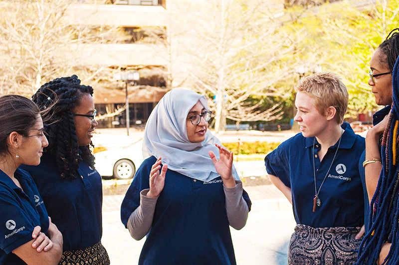 A group of five AmeriCorps members discuss their work outdoors.