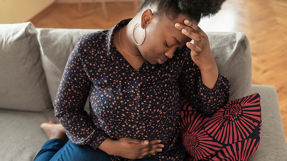 Woman on couch holding stomach and forehead, due to IC pain and discomfort.