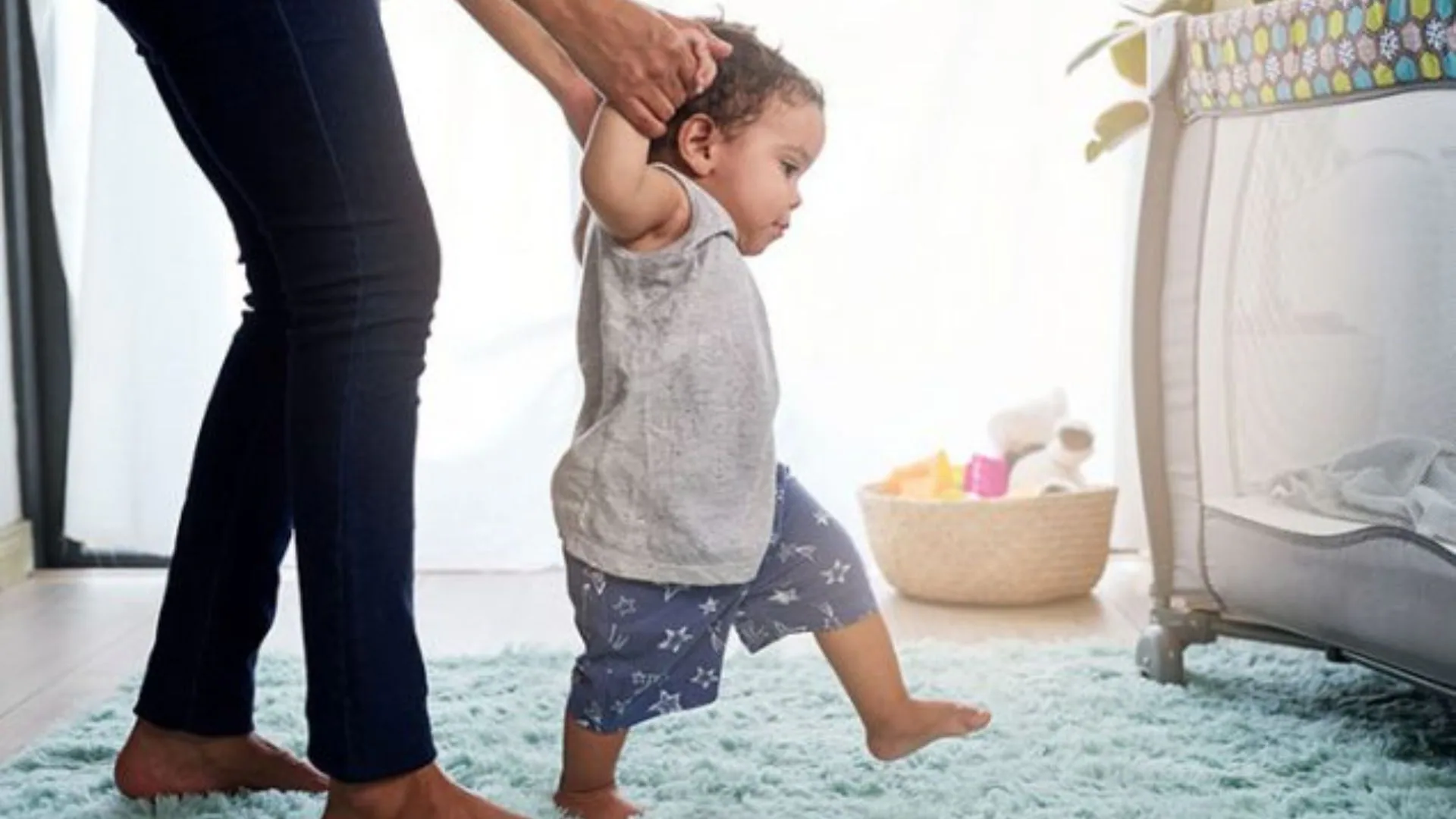 A mom holds hands and helps her child take their first steps.