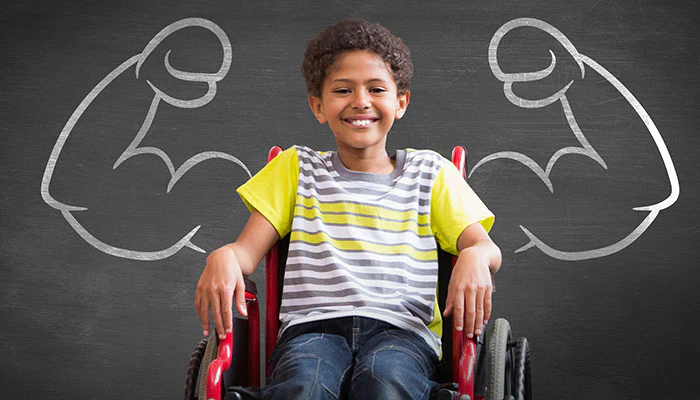 Smiling young boy in wheelchair with muscular arms drawn in chalk on blackboard behind him