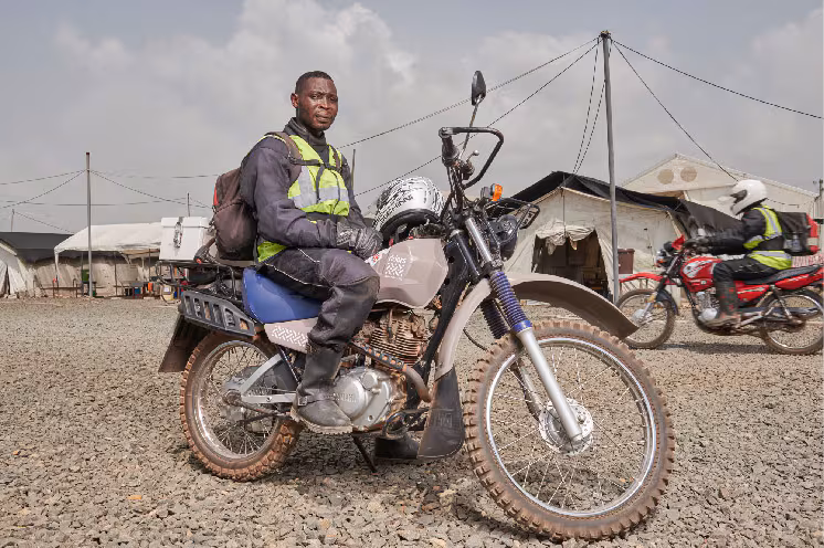 A motorcycle courier sitting on his motorcycle at a drop-off or pick-up location.
