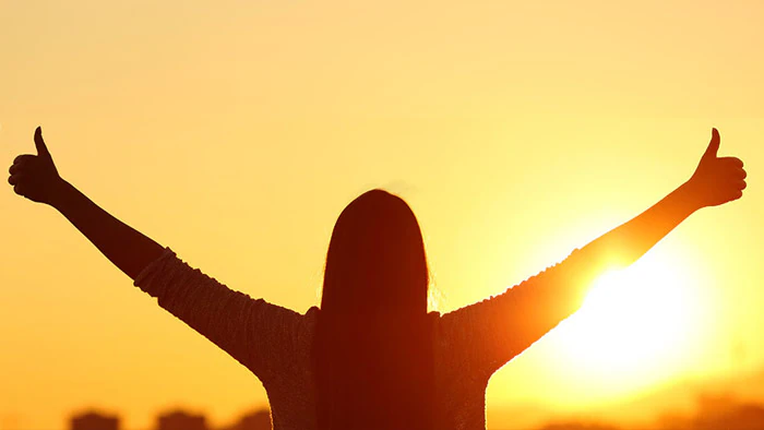 Silhouette of a teen outside during sunset, arms outstretched with thumbs up.