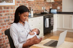 Mother Working On Laptop Holds Newborn Son And Sends Text