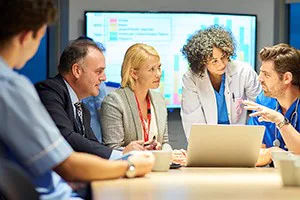 Hospital management, administrative staff, physician, and nurse listening to another nurse talking.