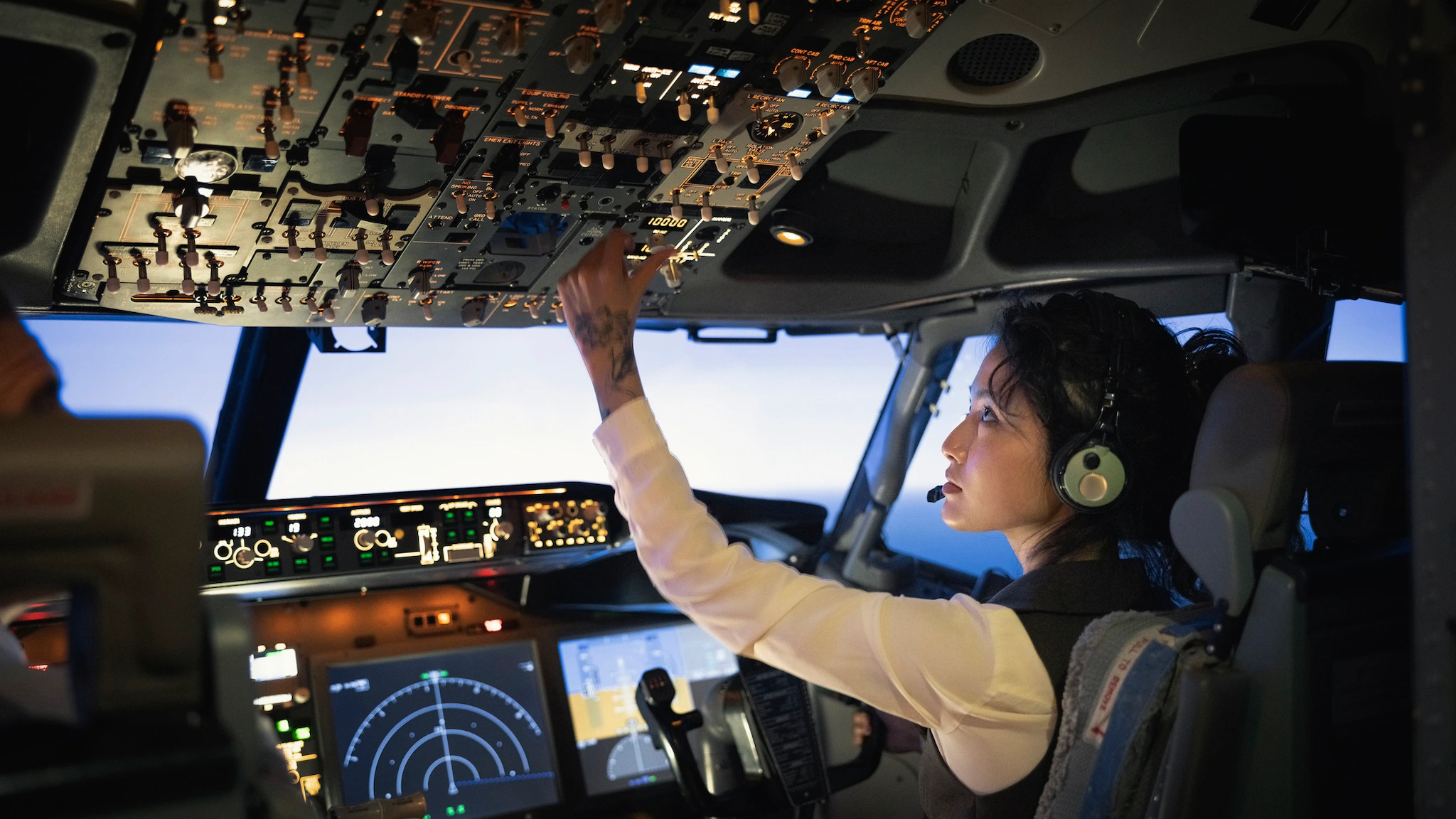 Rear view of a female pilot adjusting switches on the control panel while sitting inside cockpit.