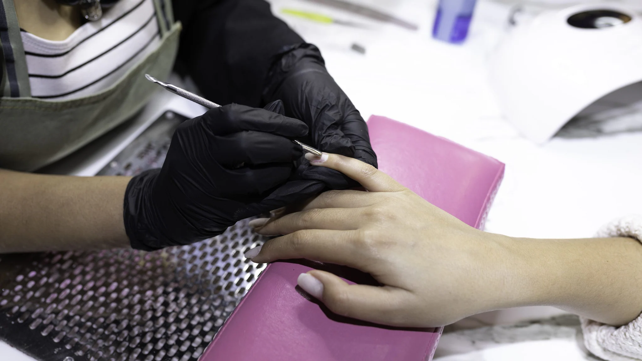 Nail technician wearing gloves and performing manicure over ventilated table