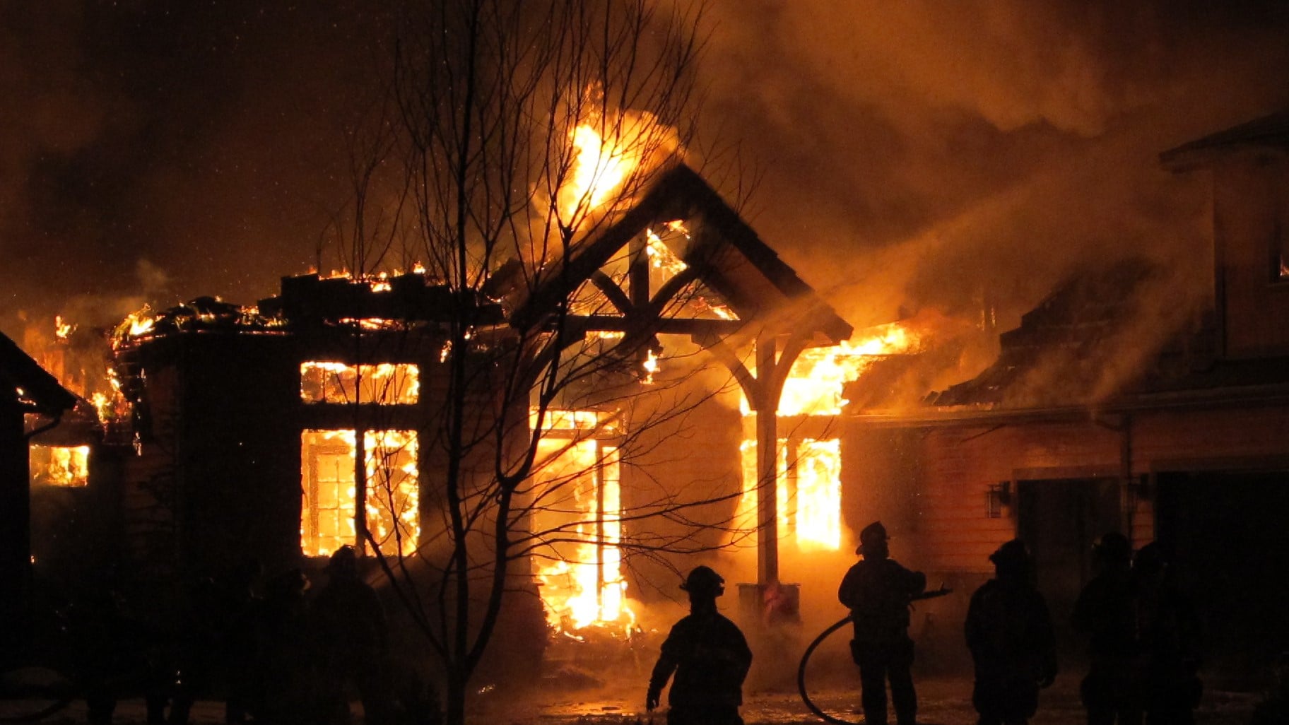 A structure on fire in the background with the silhouettes of firefighters in the foreground.