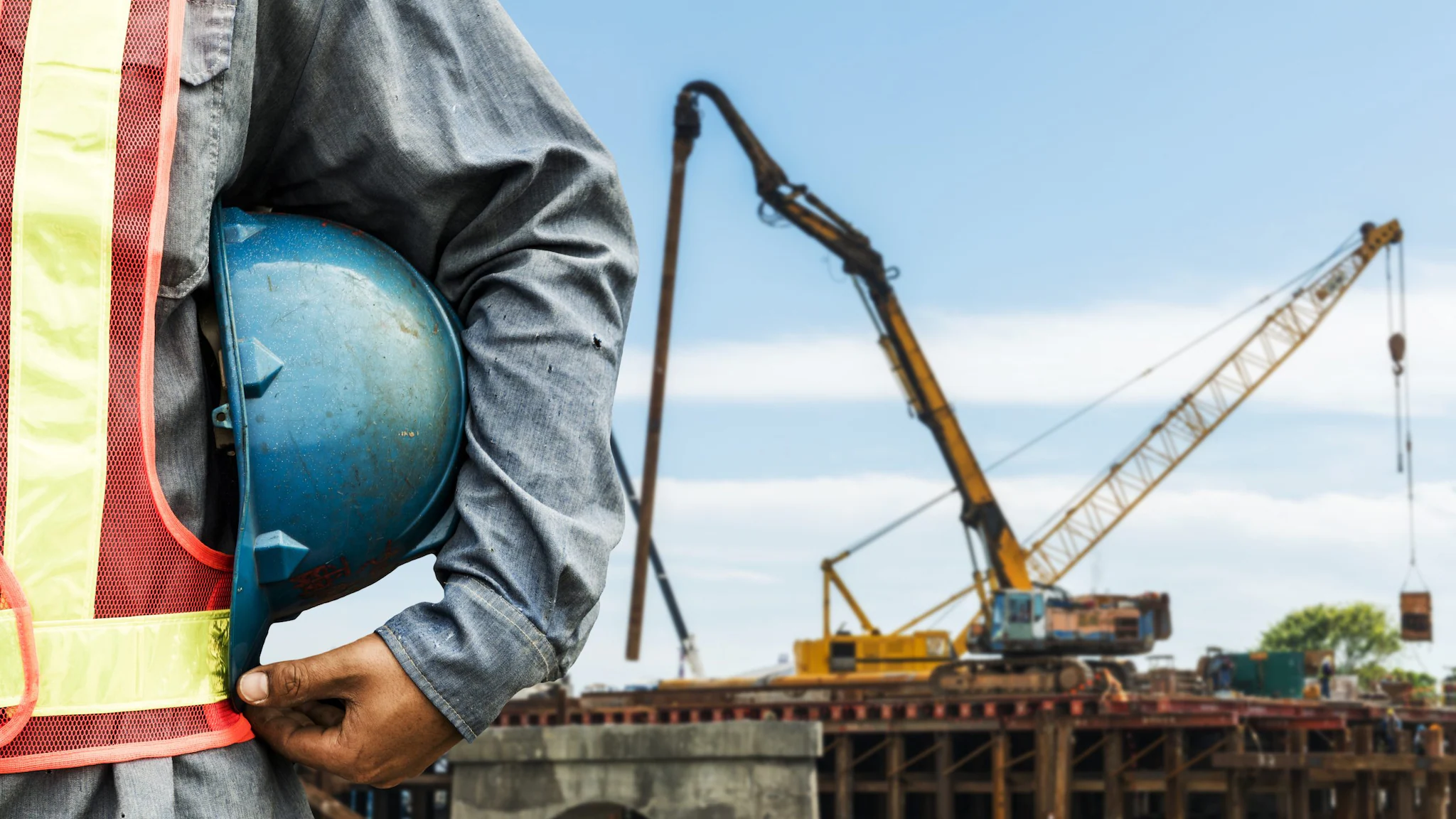 Man holding a blue construction hat with a crane in the background