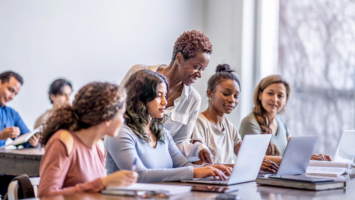 Four students with laptops interact with professor