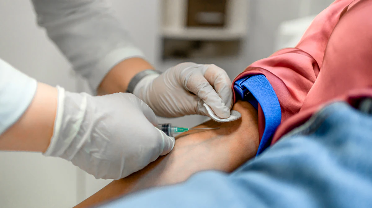 Gloved hands drawing blood from patient's arm.