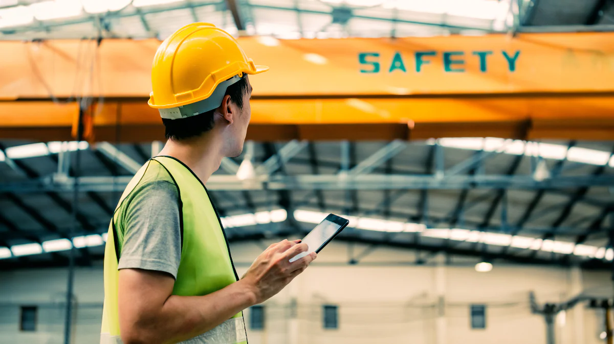 Man with hard hat and safety vest walking under a sign that says safety