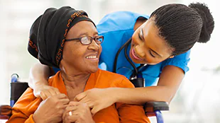 An older woman  is embraced from behind by a  medical professional