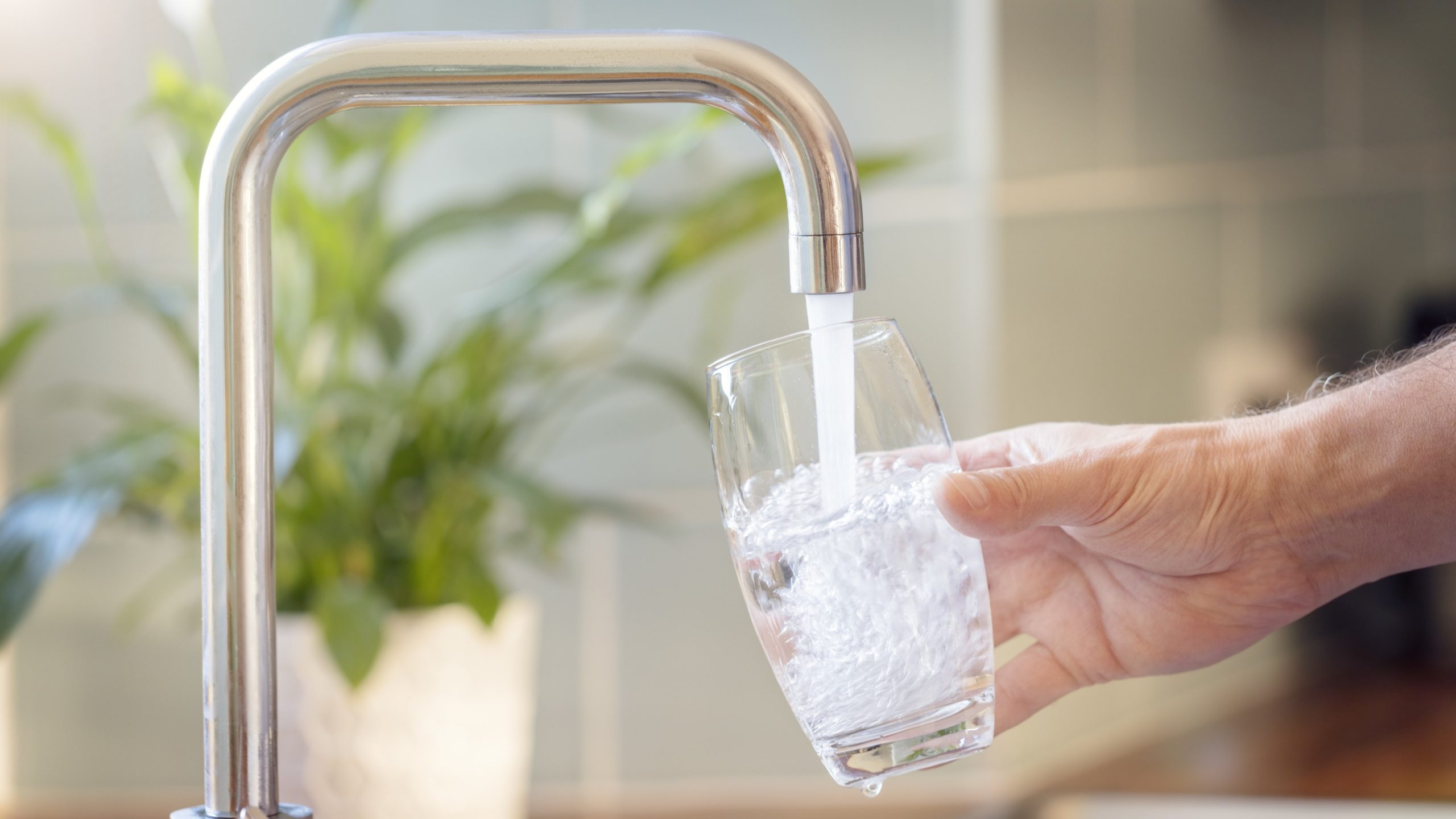 Silver faucet pouring water into a clear glass.