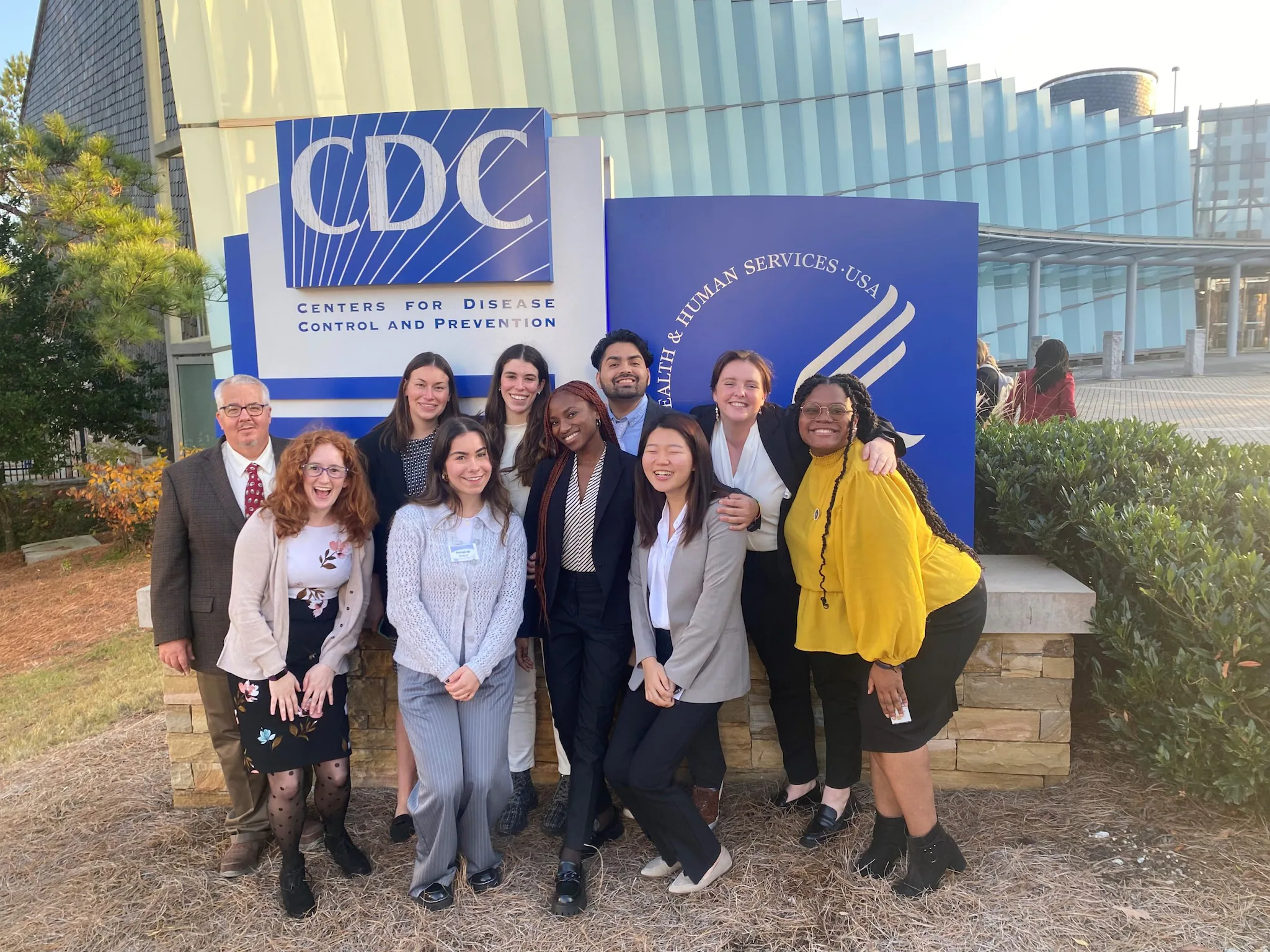 A group of associates smiles in front of the CDC headquarters sign.