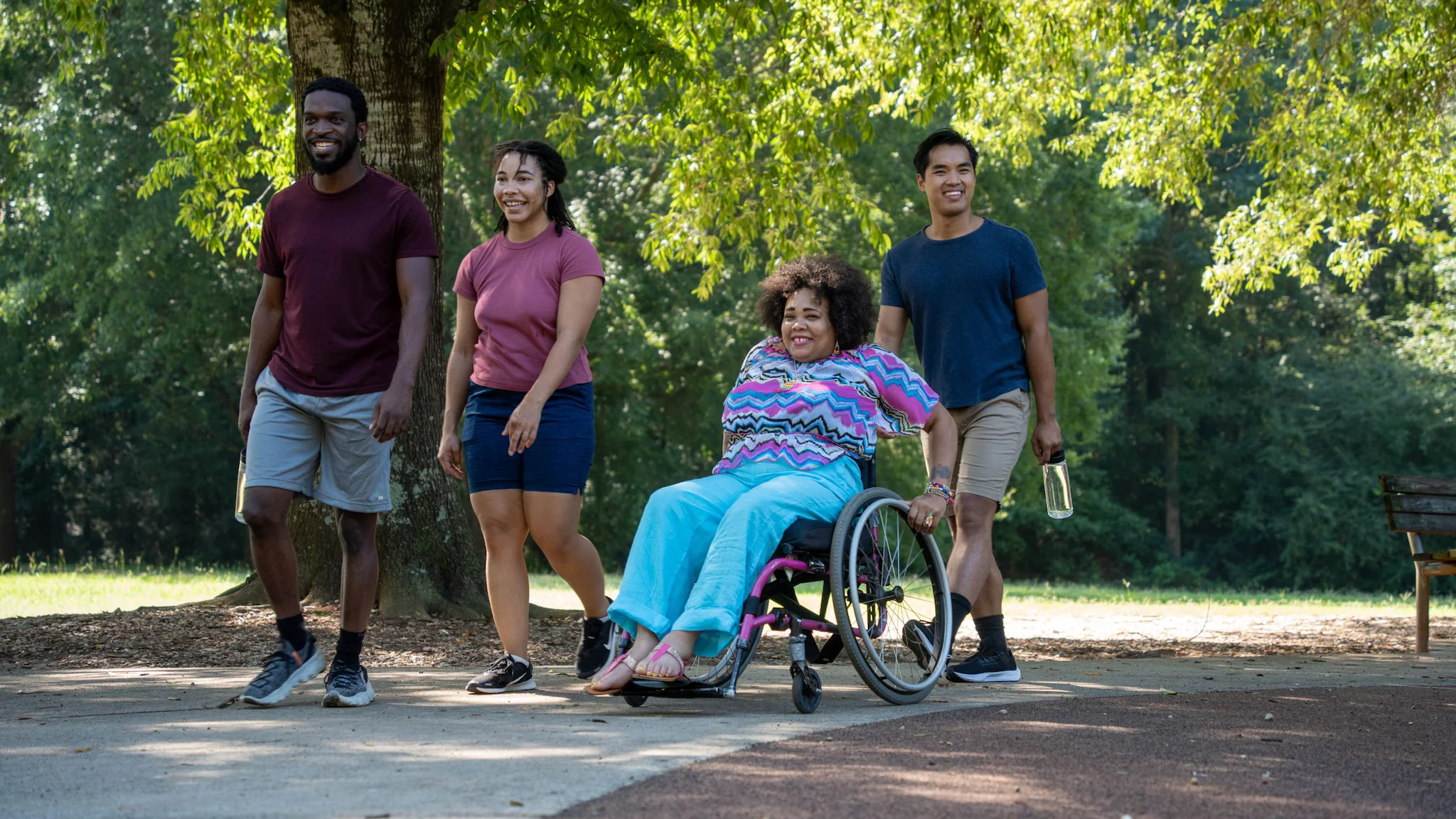 A diverse group of young people walking and rolling a wheelchair through a park