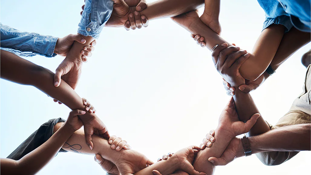 Image, from below, of people linking arms to create a circle.