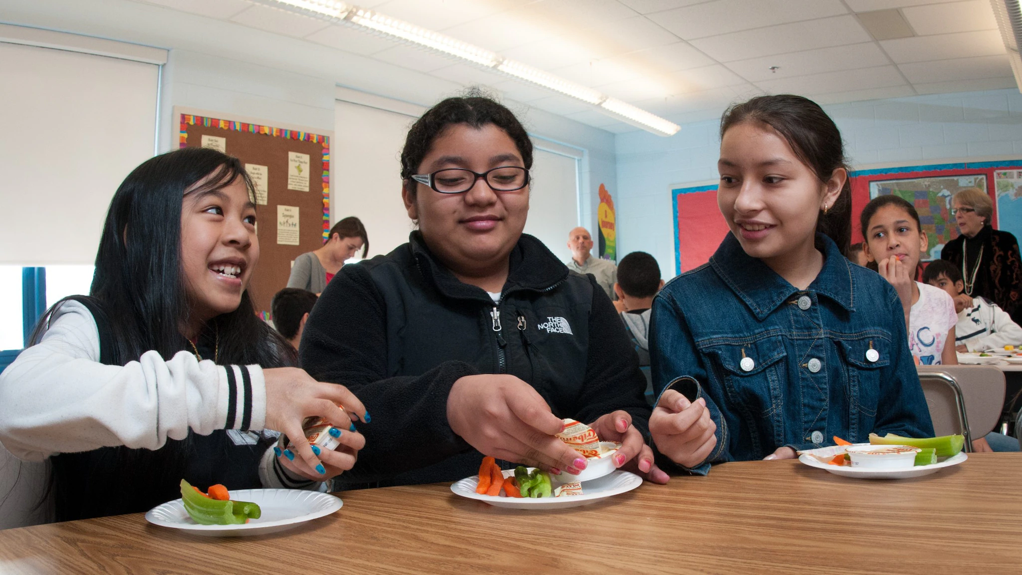 Students tasting raw vegetables with hummus in a school cafeteria.