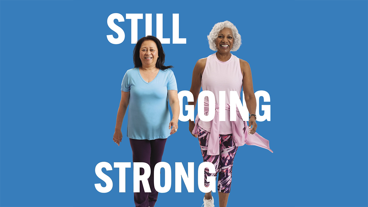 Two older women, wearing athletic clothing, walking together.