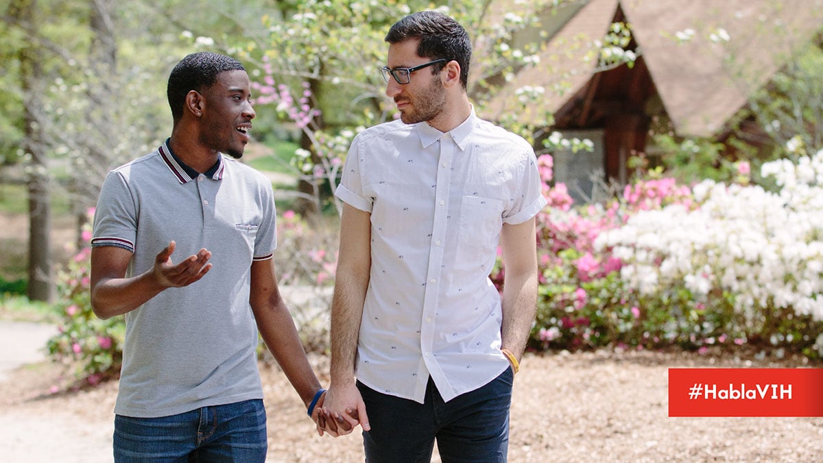 Two men walking holding hands while outside in a garden. #HablaVIH