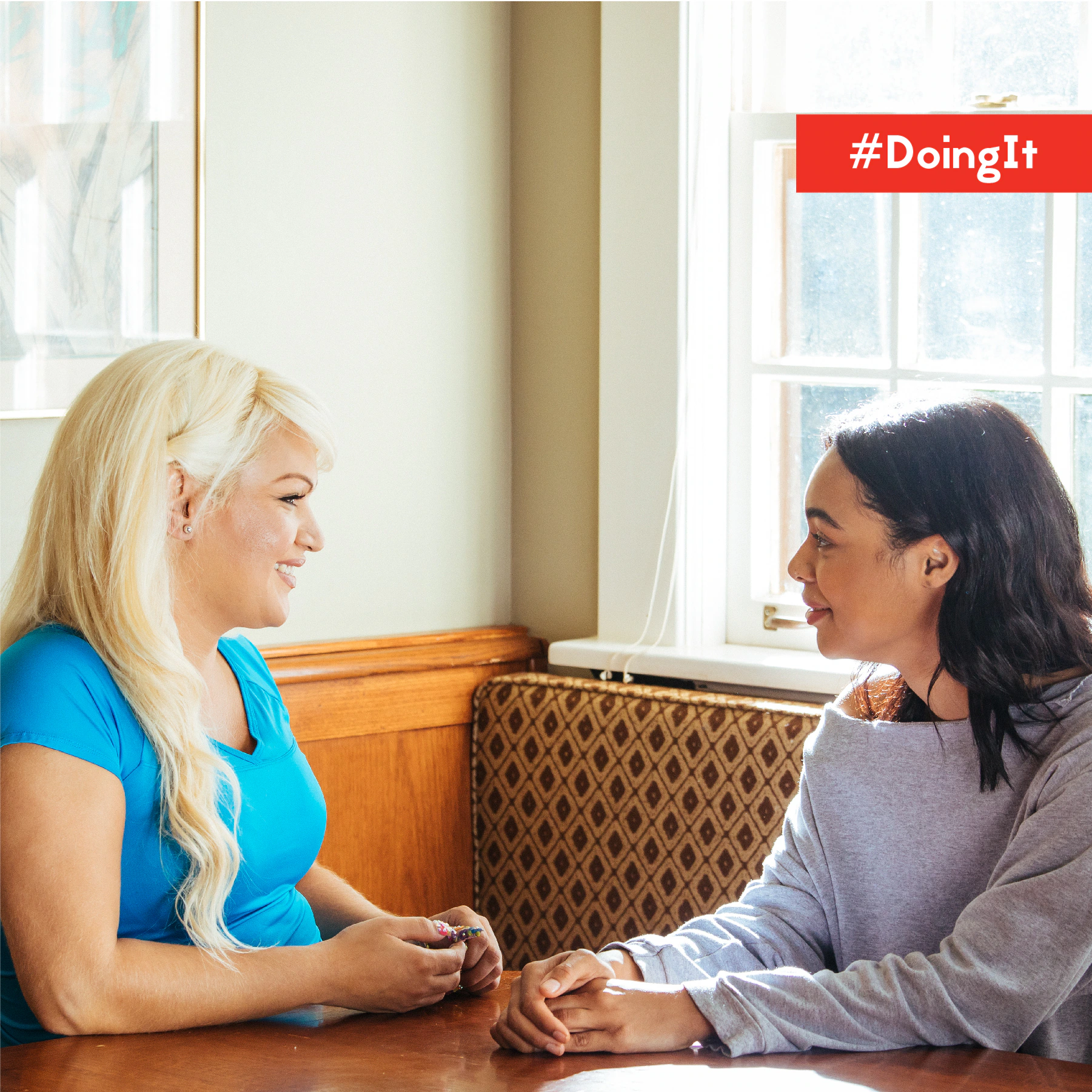 Image displays two women sitting at a table engaged in a friendly conversation.