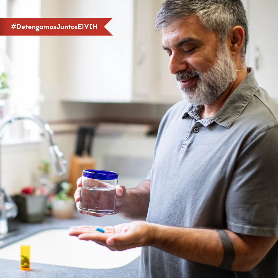 Una imagen de un hombre sosteniendo su píldora de PrEP en una mano y su vaso de agua en la otra mientras está en la cocina.