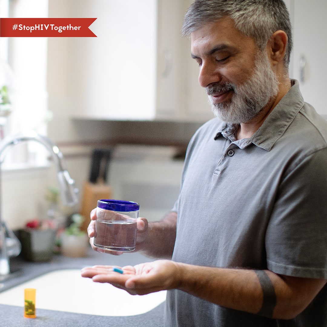 An image of a man taking a pill with with a glass of water.