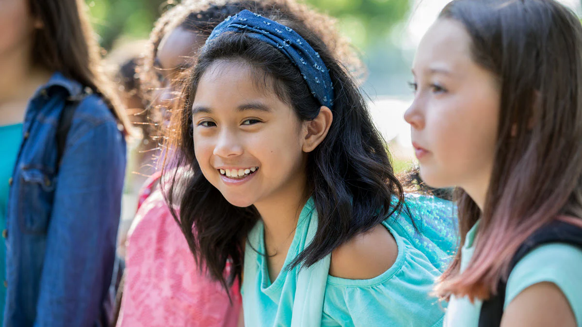 Smiling girl is wearing a backpack outside school