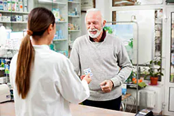 Hombre sonriente recibiendo medicación de su farmacéutico.